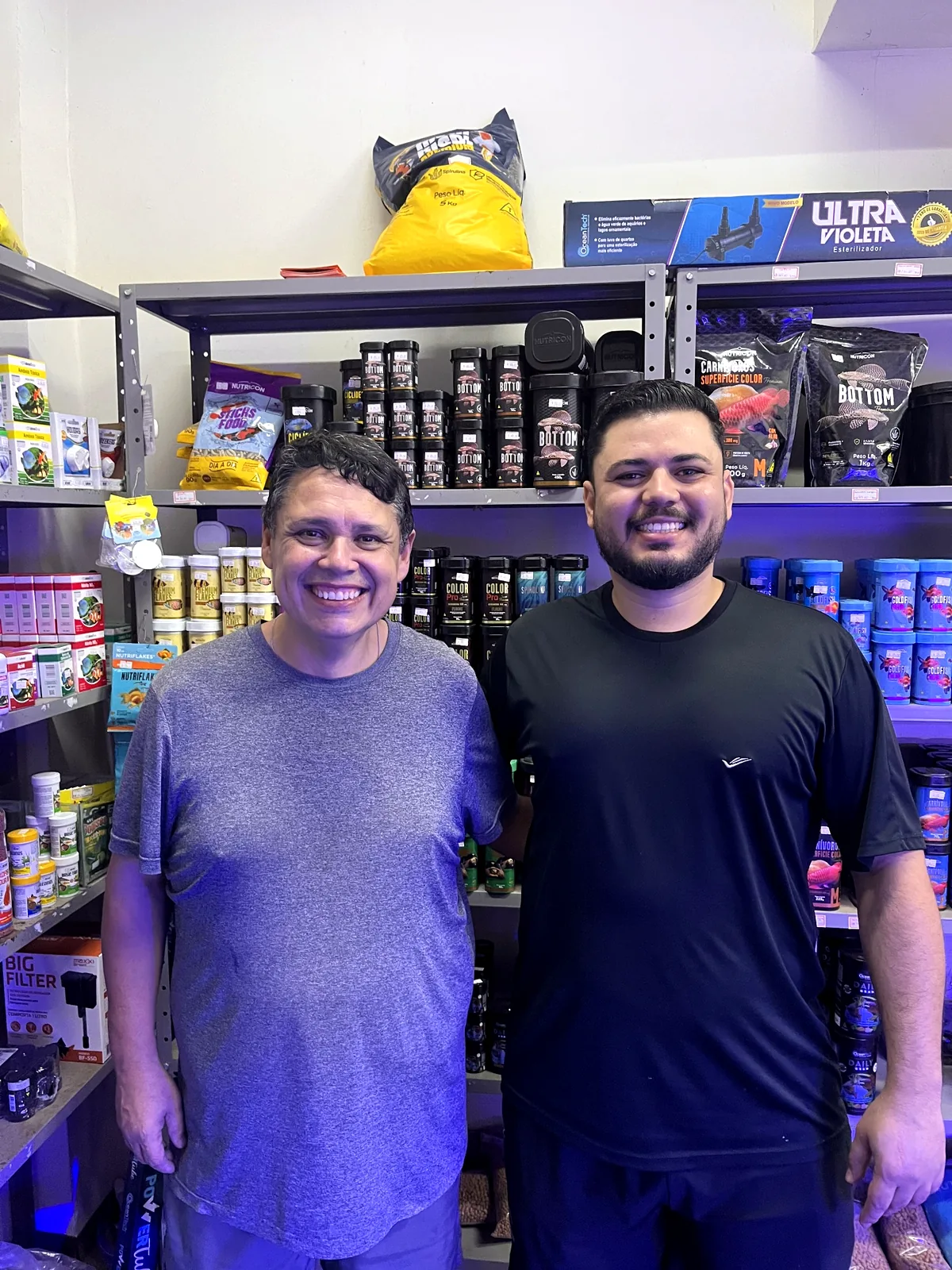 Duas pessoas na loja, em frente às prateleiras de produtos para aquarismo