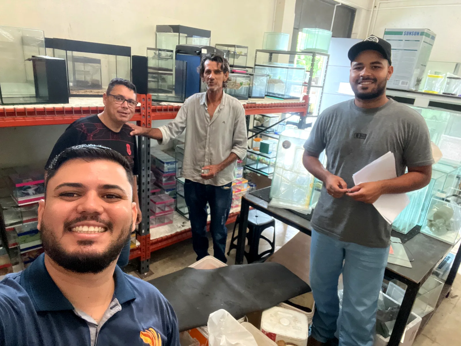 Grupo de pessoas em uma visita à loja, entre aquários de vidro e equipamentos